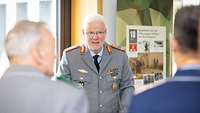Ein Mann in Uniform steht an einem Pult und spricht zu einer Menschengruppe.
